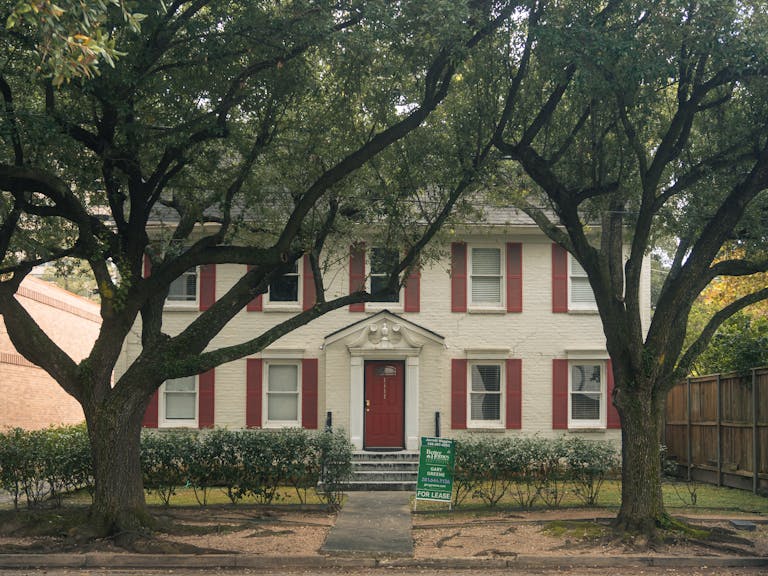 Classic colonial house with red shutters and trees in Houston, Texas, available for lease.